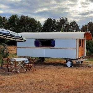 Caravane vintage sur un terrain verdoyant, avec parasol et table en bois.