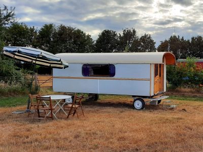 Caravane vintage sur un terrain verdoyant, avec parasol et table en bois.