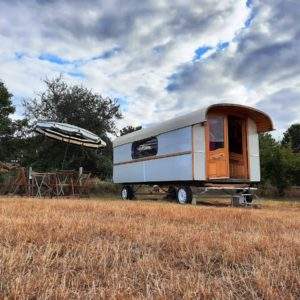 Caravane vintage dans un champ, avec une table et un parasol pour se détendre.