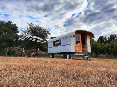 Caravane vintage dans un champ, avec une table et un parasol pour se détendre.