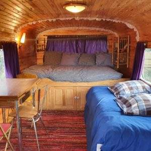 Hébergement insolite en roulotte, intérieur en bois chaleureux avec lit douillet.