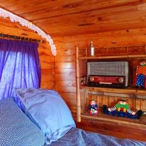 Chambre cosy dans une cabane en bois, décorée de peluches colorées et rideaux violets.
