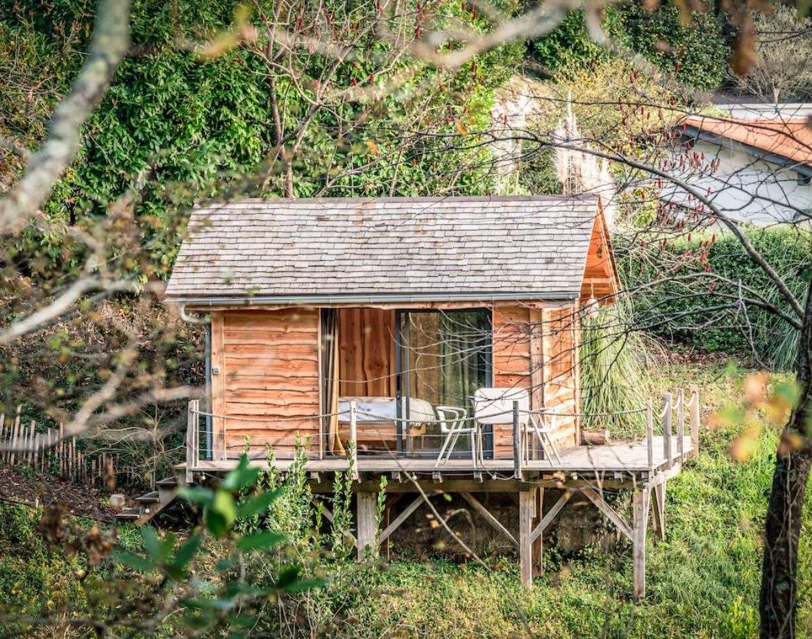 Cabane en bois sur pilotis, entourée de verdure, idéale pour un séjour insolite en Aquitaine.