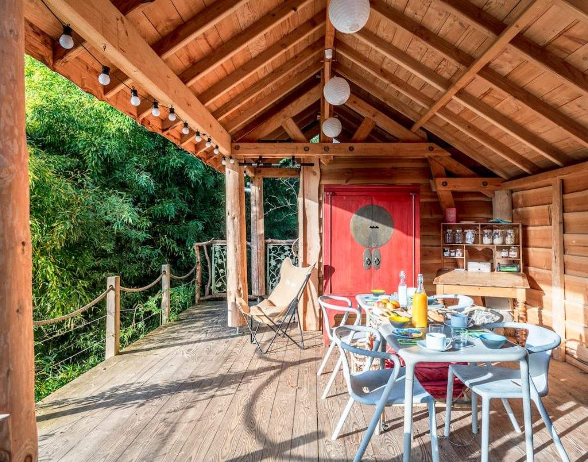 Cabane en bois avec terrasse, décorée de lanternes et vue sur la verdure.
