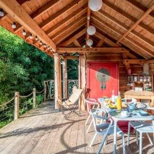 Cabane en bois avec terrasse, décorée de lanternes et vue sur la verdure.