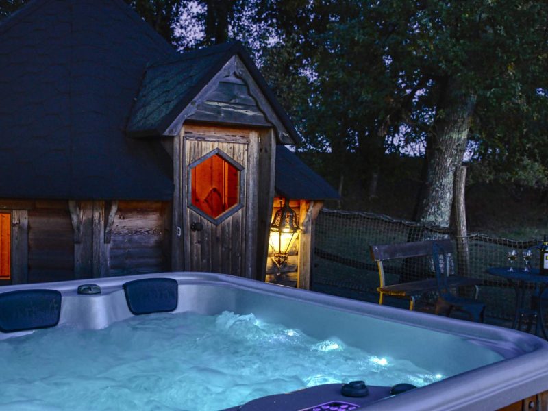 Cabane en bois avec jacuzzi illuminé, entourée de verdure paisible.