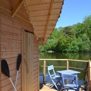 Cabane sur pilotis avec terrasse en bois, vue sur un lac paisible.