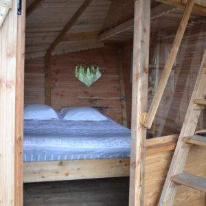 Cabane en bois avec un lit douillet et une fenêtre en forme de cœur.