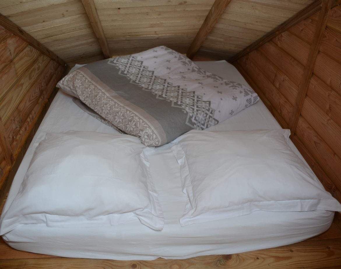 Cabane en bois avec un lit douillet et des coussins moelleux.