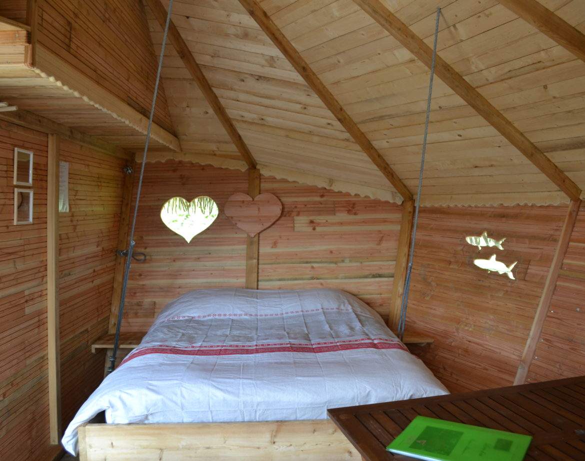 Cabane en bois avec un lit douillet et des fenêtres en forme de cœur.