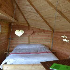 Cabane en bois avec un lit douillet et des fenêtres en forme de cœur.