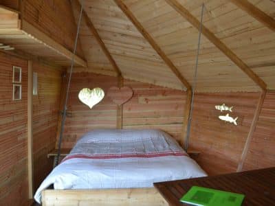 Cabane en bois avec un lit douillet et des fenêtres en forme de cœur.