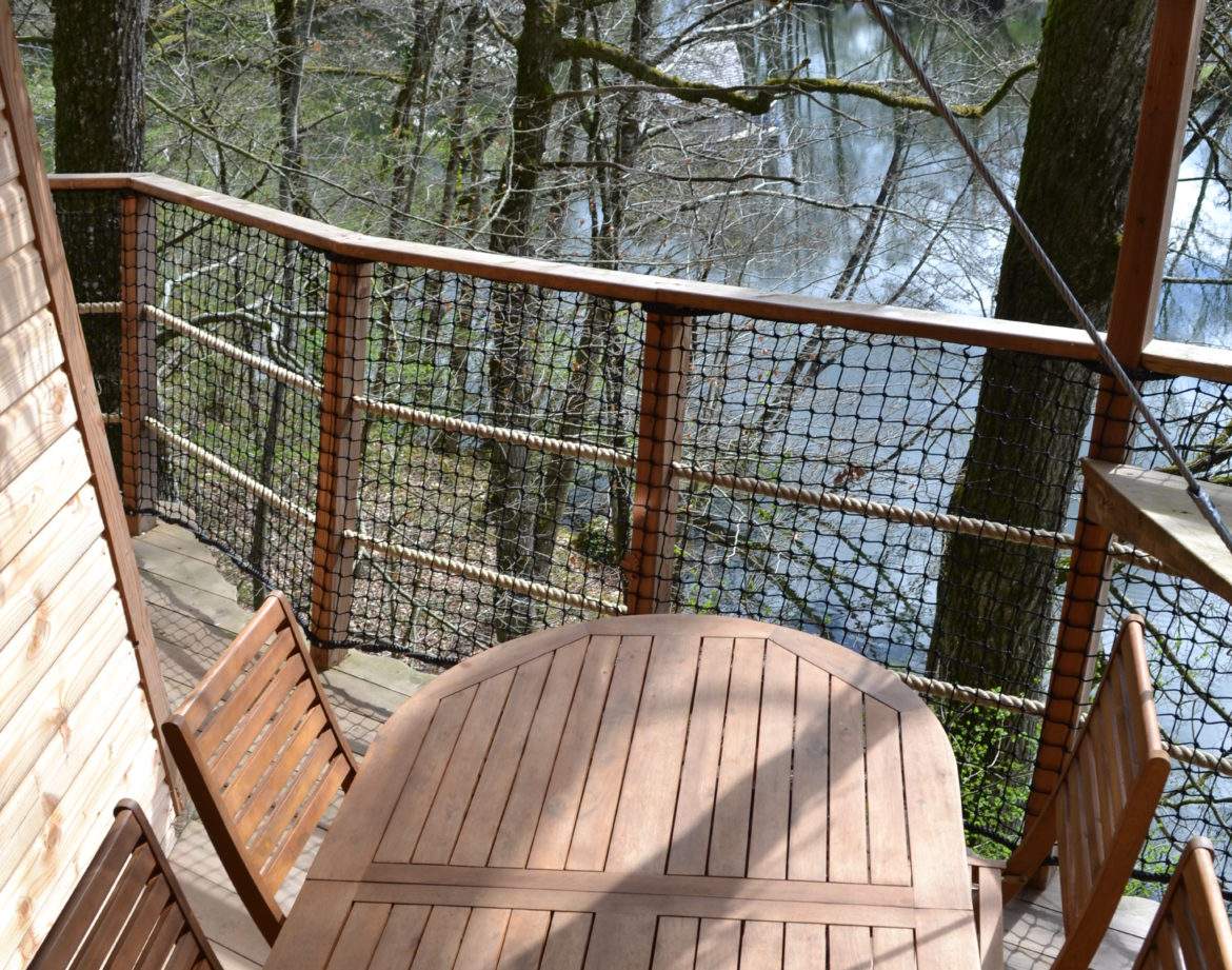 Cabane perchée dans les arbres avec terrasse en bois surplombant un étang paisible.
