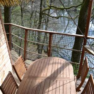Cabane perchée dans les arbres avec terrasse en bois surplombant un étang paisible.
