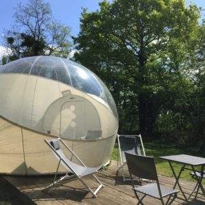Hébergement insolite en bulle transparente, avec terrasse et chaises en bois.