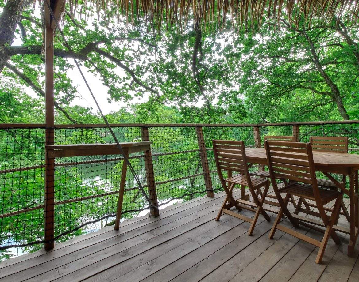 Cabane perchée dans les arbres avec terrasse en bois et vue sur la nature verdoyante.