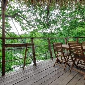 Cabane perchée dans les arbres avec terrasse en bois et vue sur la nature verdoyante.