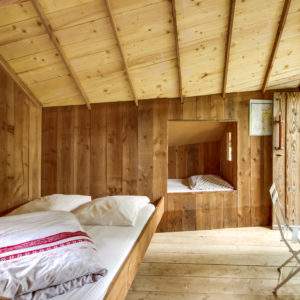 Cabane en bois chaleureuse avec lits confortables et lumière naturelle.