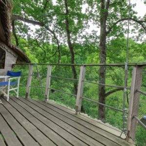 Cabane perchée dans les arbres avec terrasse en bois et vue sur la nature verdoyante.
