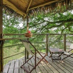 Cabane perchée dans un arbre, avec chaises longues et vue sur la nature environnante.
