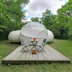 Bulle transparente dans la nature, avec terrasse en bois et mobilier de jardin.