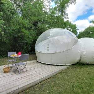 Bulle transparente dans la nature, avec terrasse en bois et mobilier de jardin.