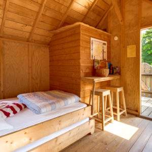 Cabane en bois lumineuse avec lit confortable et vue sur la nature.