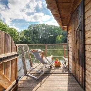 Cabane sur pilotis avec terrasse en bois surplombant un étang paisible.