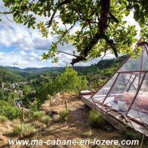Cabane en verre sur pilotis, offrant une vue panoramique sur la vallée verdoyante.