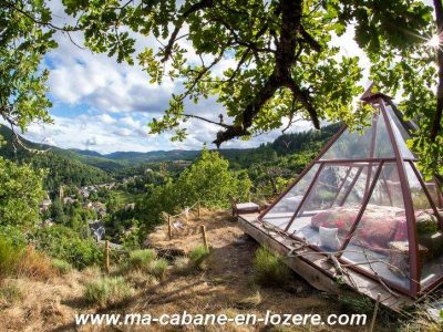 Cabane en verre sur pilotis, offrant une vue panoramique sur la vallée verdoyante.