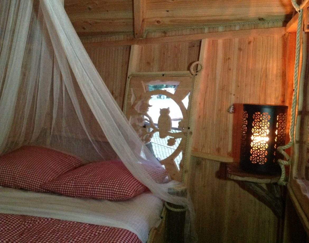 Cabane en bois avec lit à baldaquin et lumière tamisée, ambiance chaleureuse.