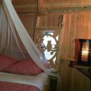 Cabane en bois avec lit à baldaquin et lumière tamisée, ambiance chaleureuse.