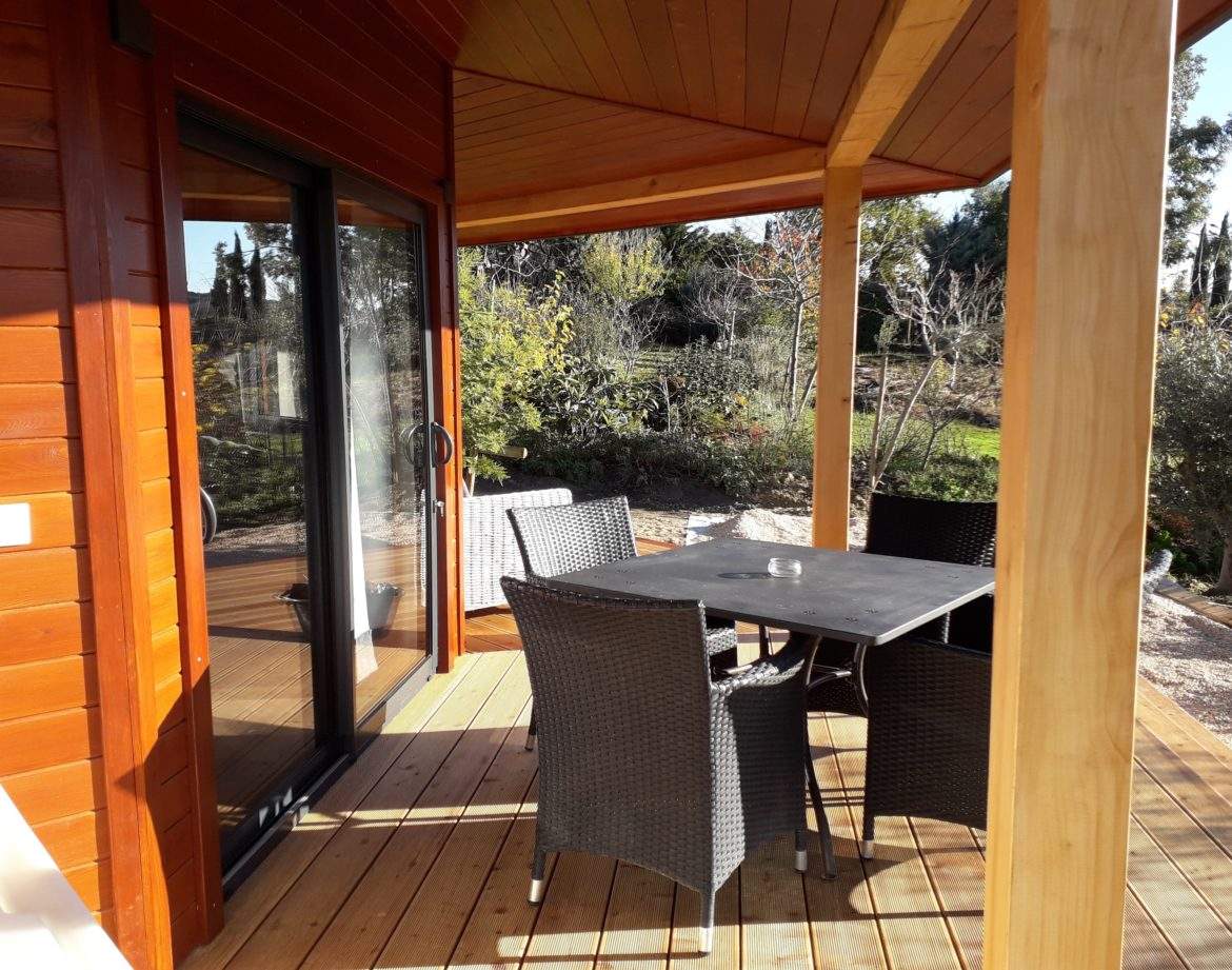 Chalet en bois avec terrasse ensoleillée et mobilier extérieur confortable.