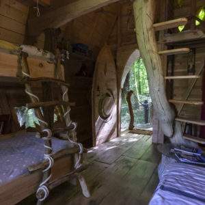 Cabane en bois dans les arbres, avec un escalier en rondins et une vue sur la forêt.
