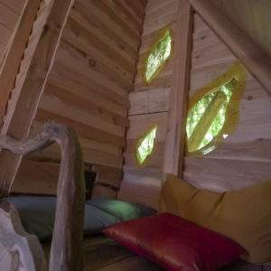 Cabane en bois avec des fenêtres en forme de feuilles et un intérieur chaleureux.