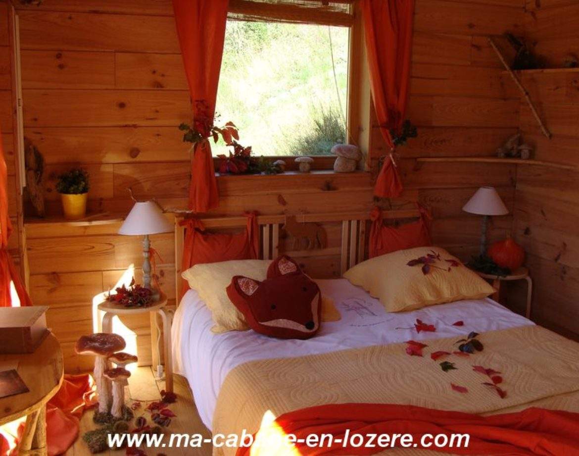 Cabane en bois chaleureuse avec lit douillet et décor automnal accueillant.