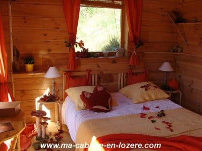Cabane en bois chaleureuse avec lit douillet et décor automnal accueillant.