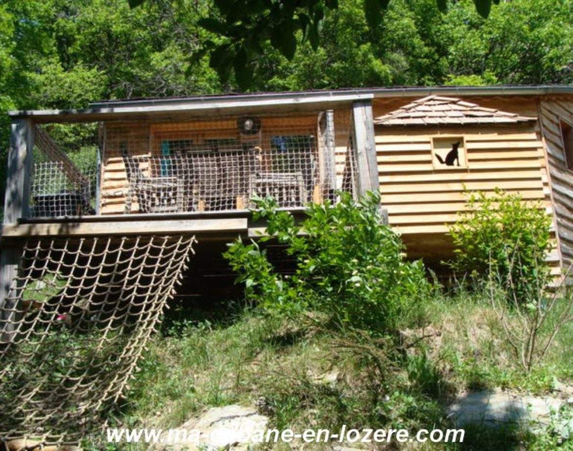 Cabane en bois perchée, entourée de verdure, avec une terrasse en bois accueillante.