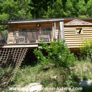 Cabane en bois perchée, entourée de verdure, avec une terrasse en bois accueillante.