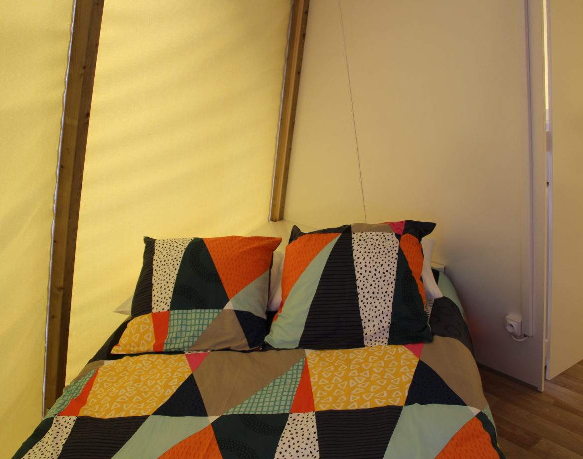 Tente lodge colorée avec un lit douillet et des coussins géométriques.