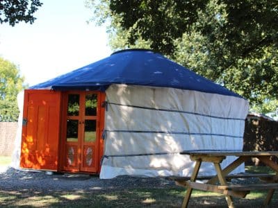 Yourte colorée avec porte orange, nichée dans la verdure des Pays de la Loire.