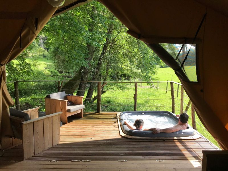 Tente de luxe avec jacuzzi sur la terrasse, vue sur la nature verdoyante.
