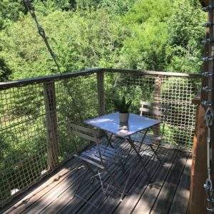 Cabane perchée avec terrasse en bois, vue sur la verdure environnante.
