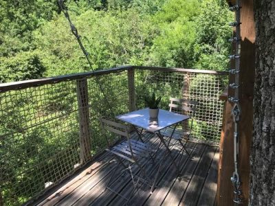 Cabane perchée avec terrasse en bois, vue sur la verdure environnante.