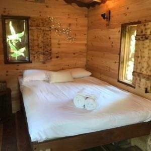 Cabane en bois cosy avec lit douillet et fenêtres laissant entrer la lumière naturelle.
