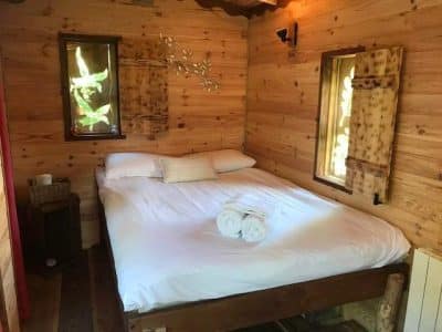 Cabane en bois cosy avec lit douillet et fenêtres laissant entrer la lumière naturelle.