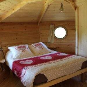 Cabane en bois avec lit douillet et fenêtres rondes, décorée de cœurs.