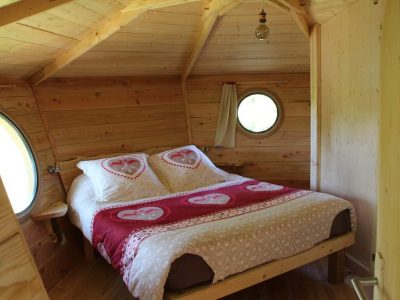 Cabane en bois avec lit douillet et fenêtres rondes, décorée de cœurs.