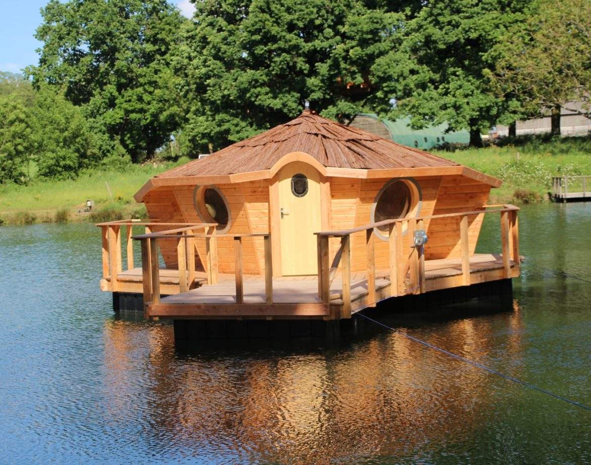 Cabane flottante en bois sur un lac, entourée de verdure luxuriante.