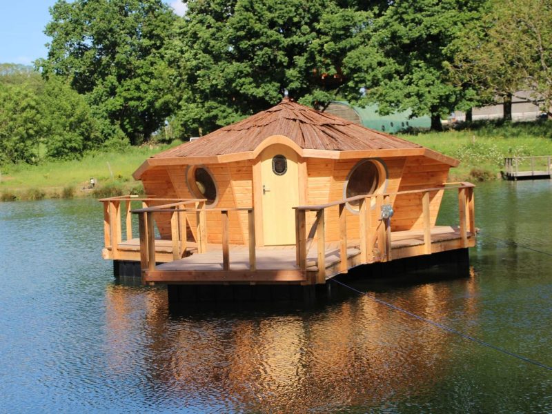 Cabane flottante en bois sur un lac, entourée de verdure luxuriante.